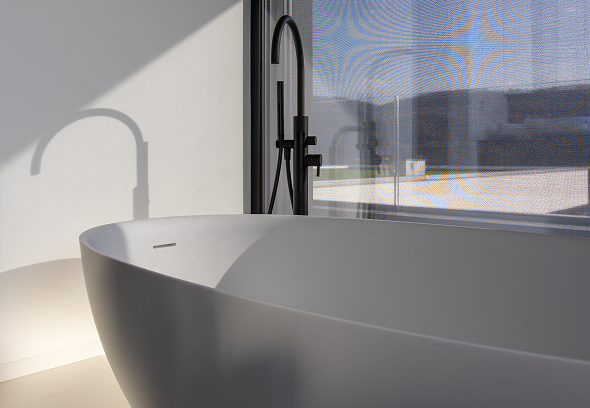 Elegante vasca da bagno da bagno bianca con rubinetto nero, finestra luminosa che proietta ombre morbide sulla parete.