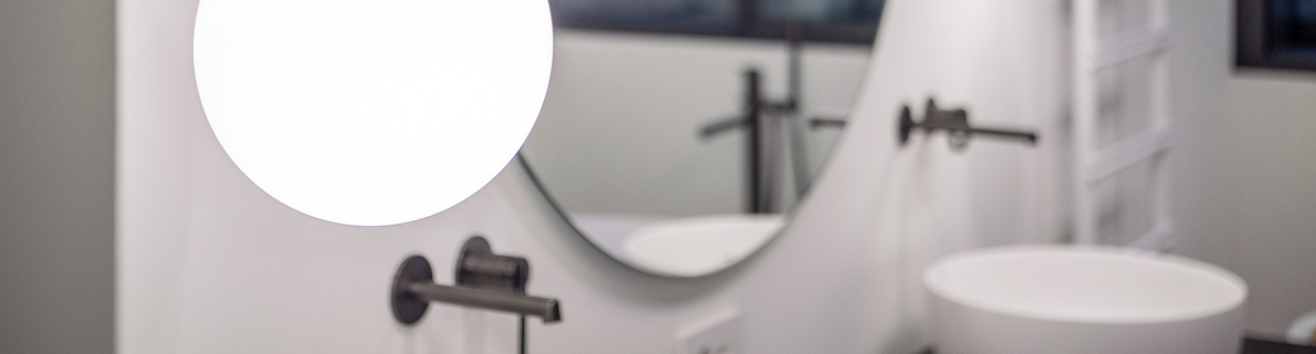 Lavabo da bagno moderno con specchio tondo e luci appese, primo piano sfocato su rubinetteria
