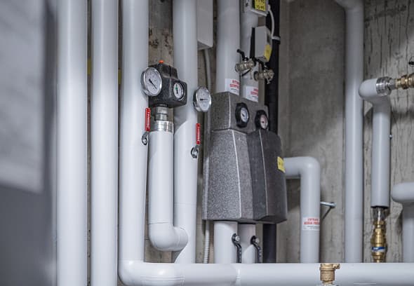 Immagine di tubazioni, valvole e strumenti di controllo in un impianto industriale, con tubazioni bianche, manometri e componenti metallici.
