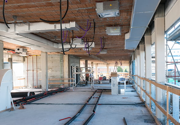 Interno cantiere edile: impalcature, tubazioni e impianti a vista lungo corridoio