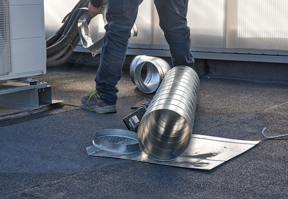 Tecnico sul tetto maneggia condotto metallico lucido e accessori: tubi, guarnizioni e piastra di fissaggio durante lavoro di manutenzione