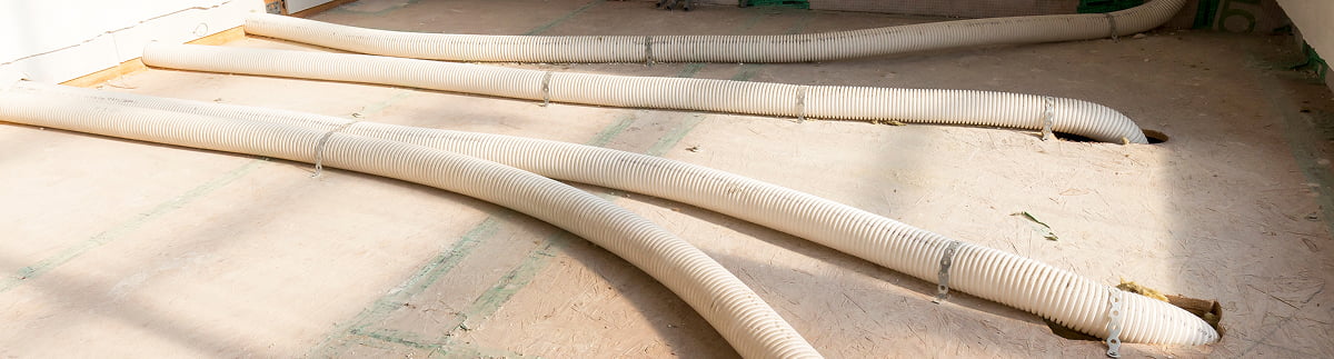 Tubazioni flessibili bianche in gomma posate su superficie pavimentata, probabilmente in cantiere o in ambiente industriale.