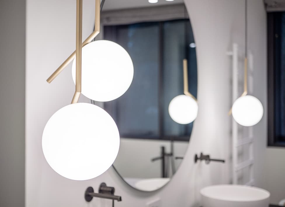 Specchio rotondo con luce soffusa, sfondo bagno moderno e lampade a globo bianche. Atmosfera minimal: riflessi delicati e design contemporaneo.